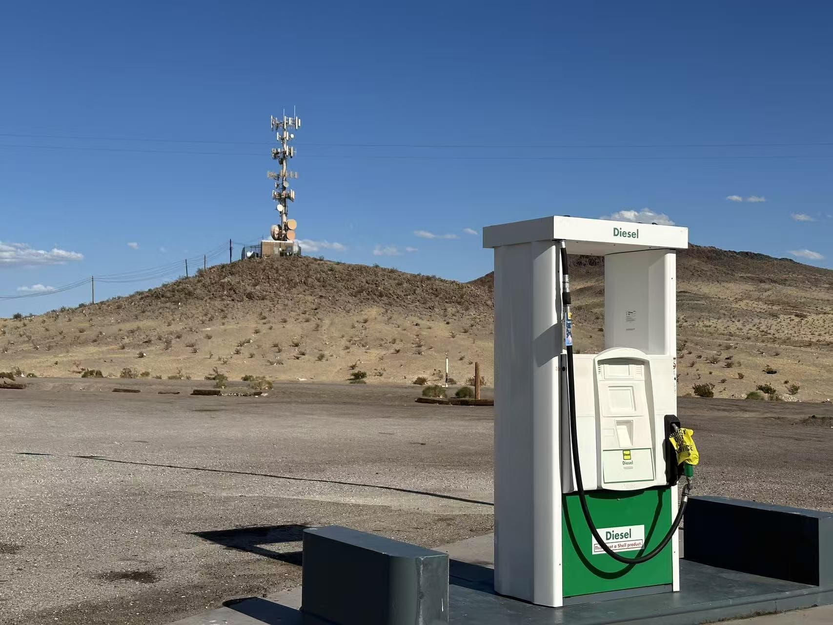 Fuel pump at a desert station below a hill with a radio mast